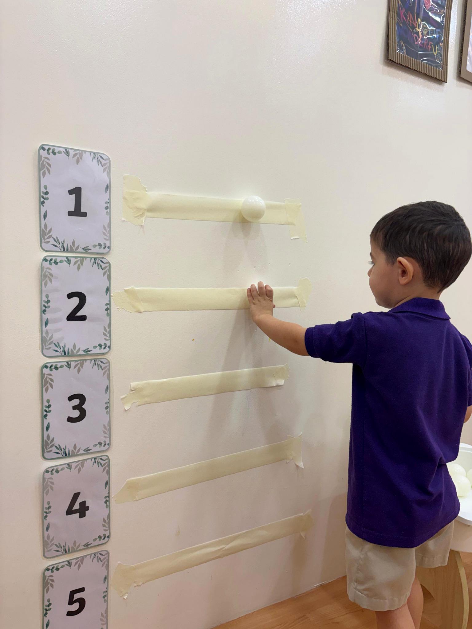 Child exploring numbers and movement with a wall-mounted ball run