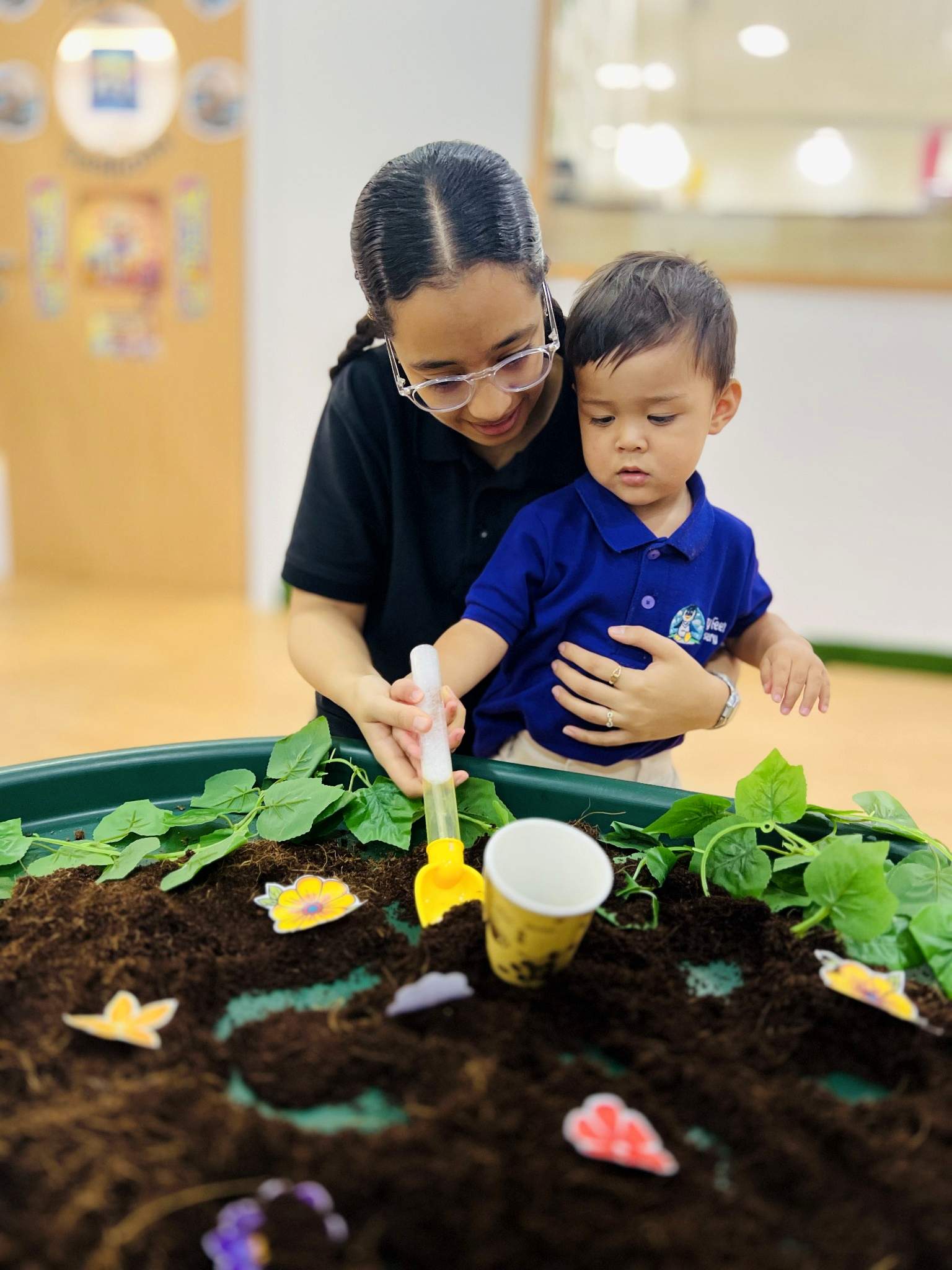 Educator supporting a child exploring plants and soil in a sensory tray