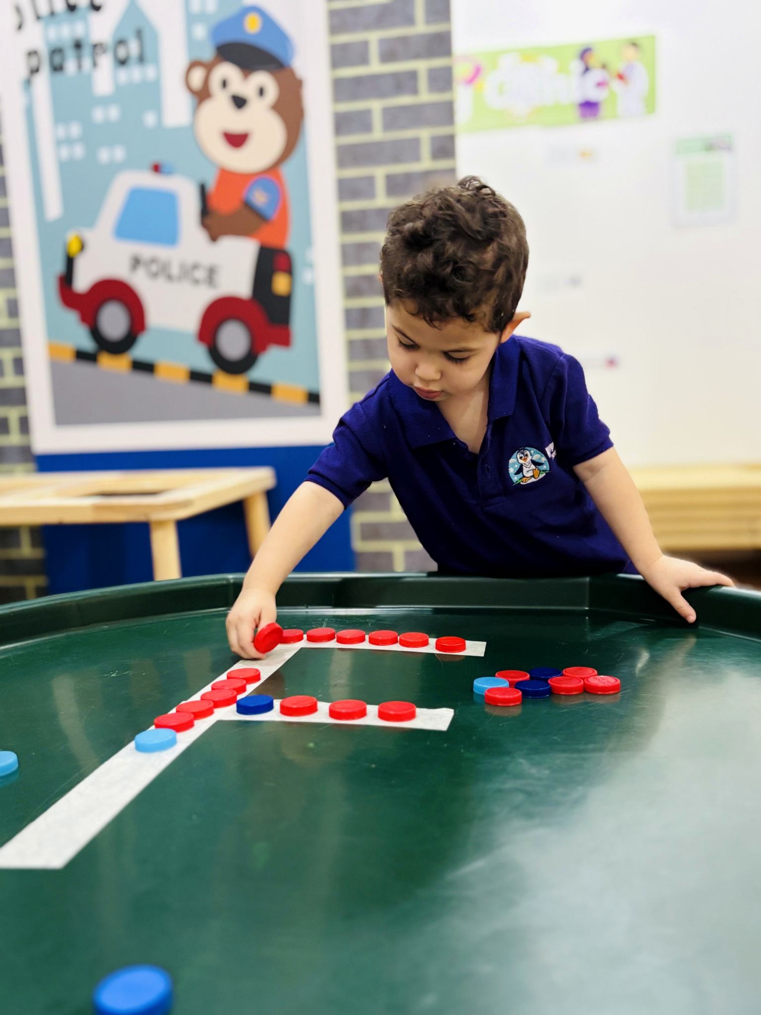 Child arranging bottle caps along a letter outline during a nursery activity