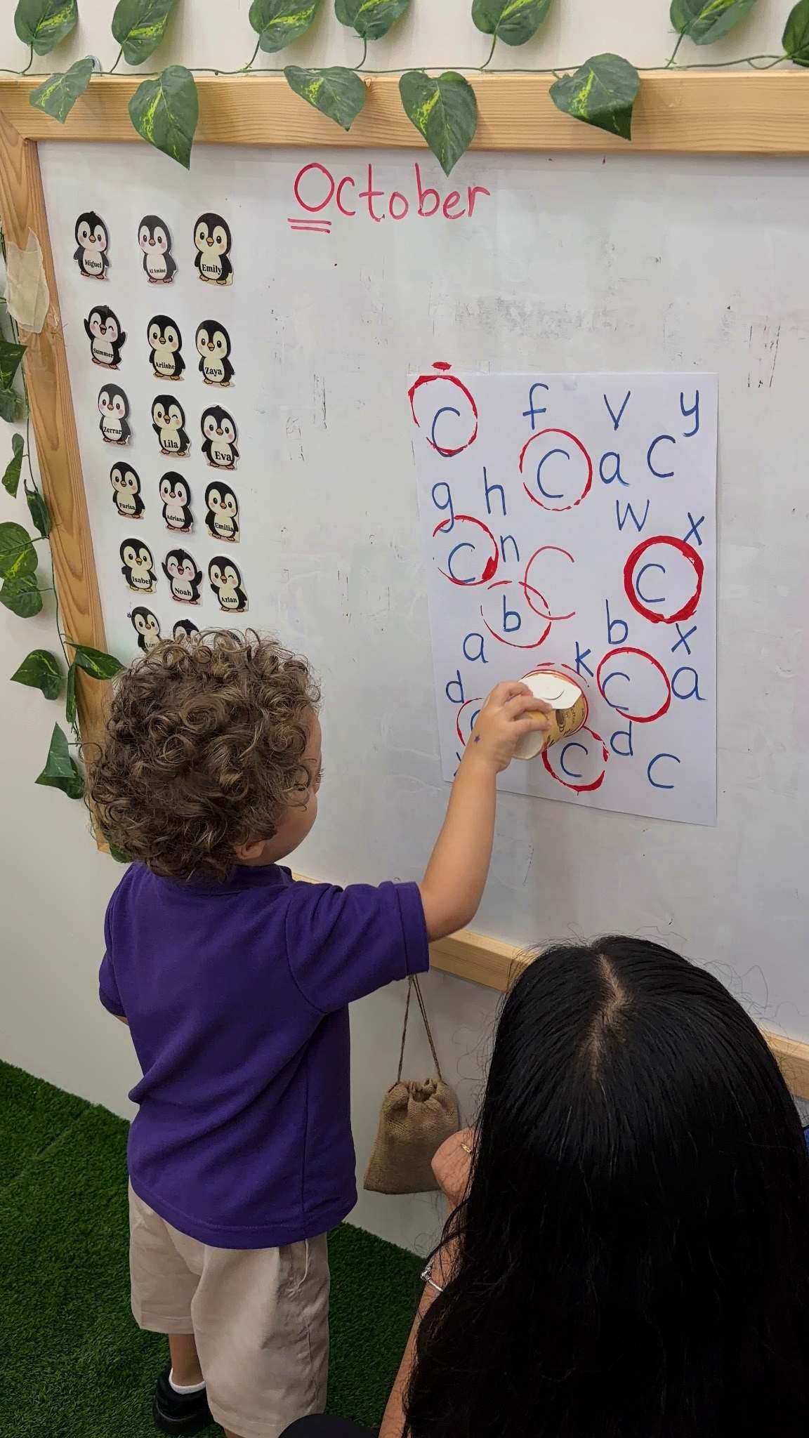 Child stamping circles around letters with an educator during a literacy activity