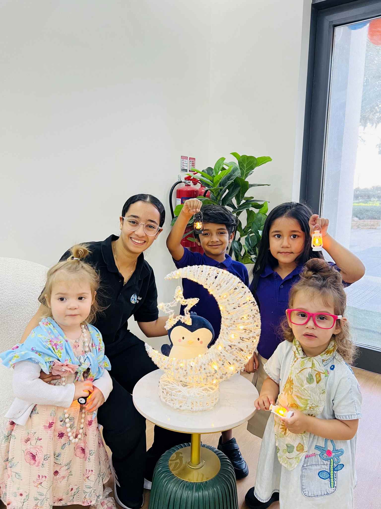 Children and an educator holding lanterns beside a crescent moon display