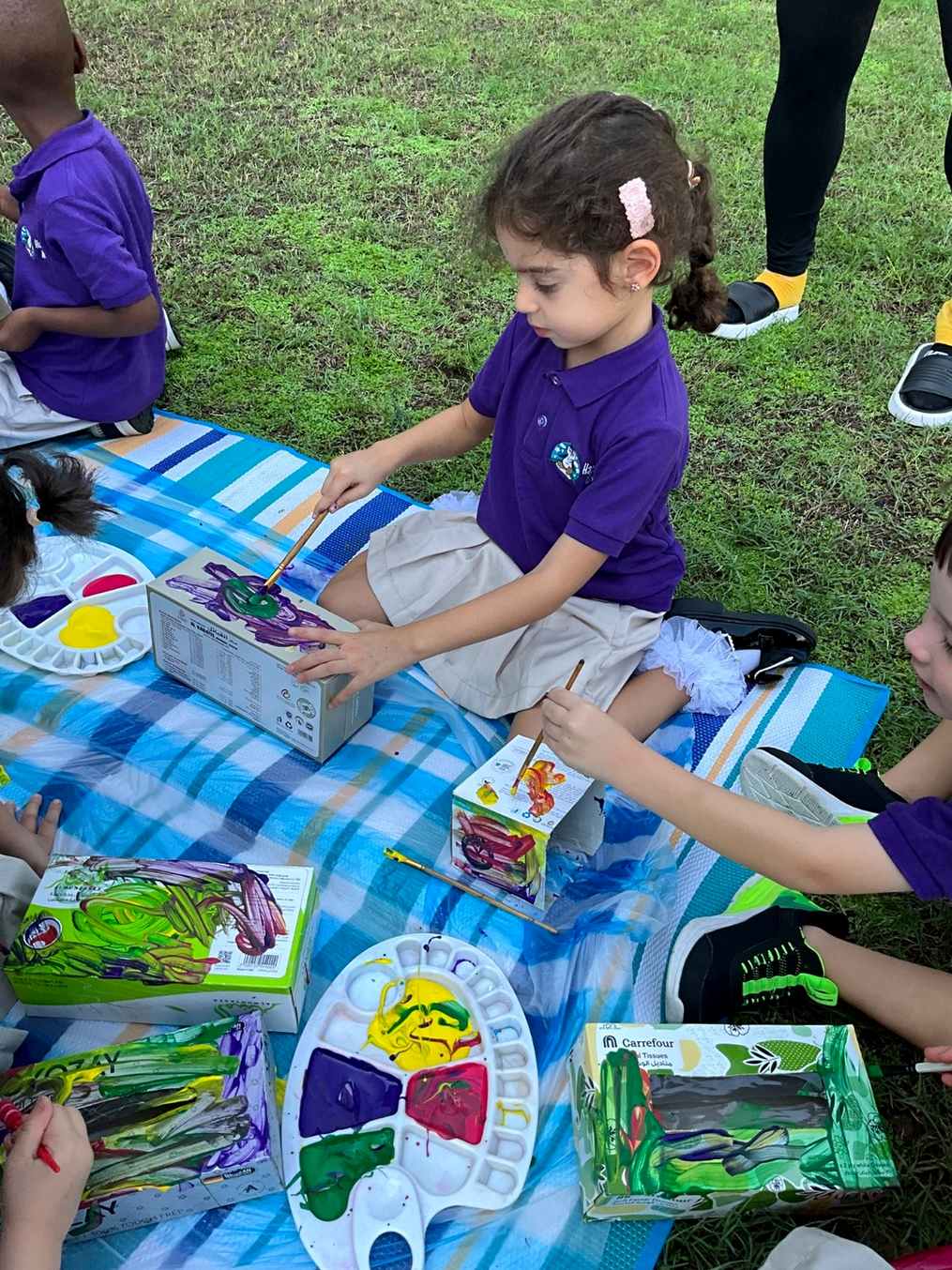 Children in nursery uniform painting recycled boxes outdoors
