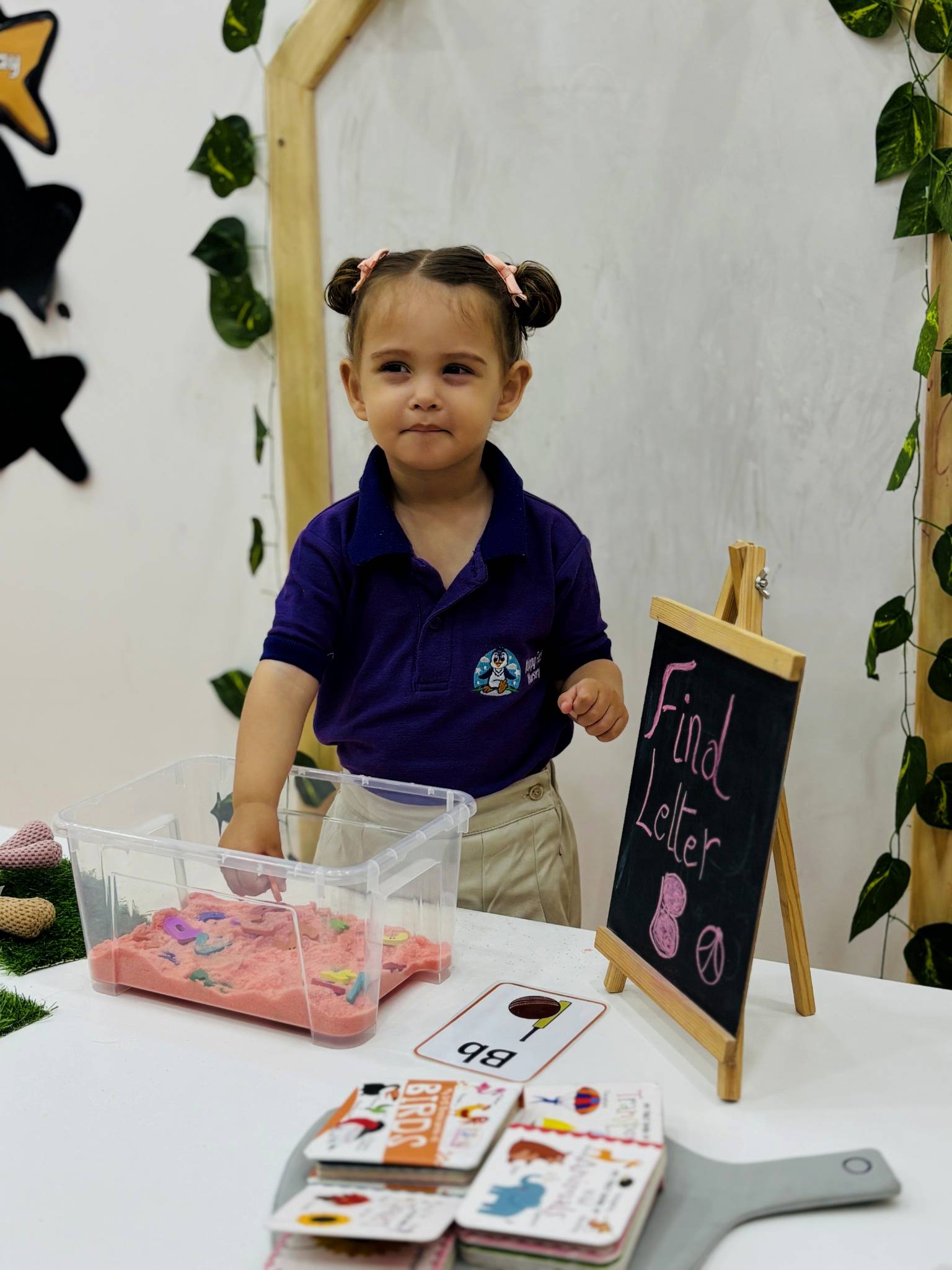 Child exploring letter shapes in a coloured sand tray at Happy Feet Nursery