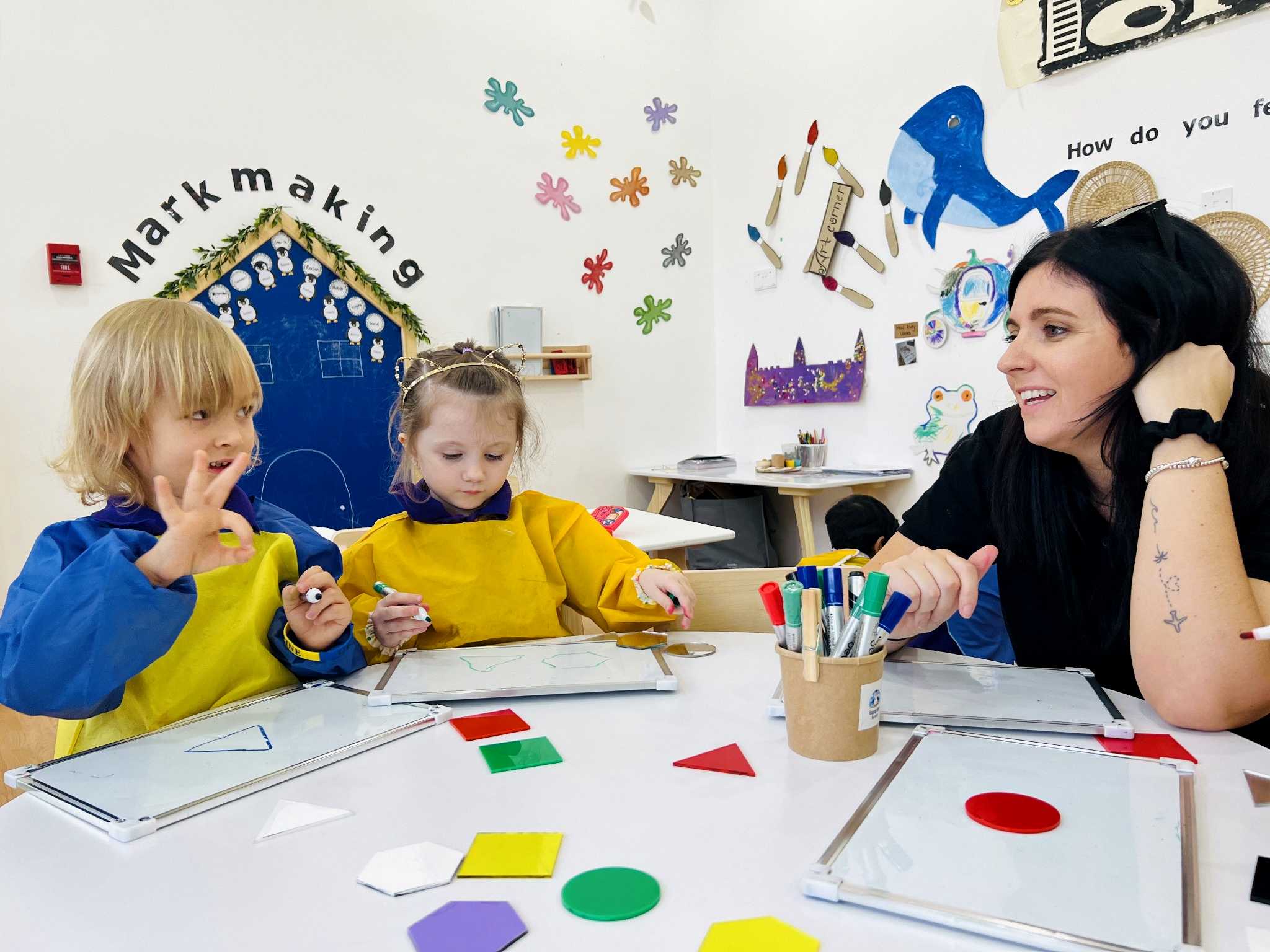 Children exploring shapes and mark making with an educator at Happy Feet Nursery