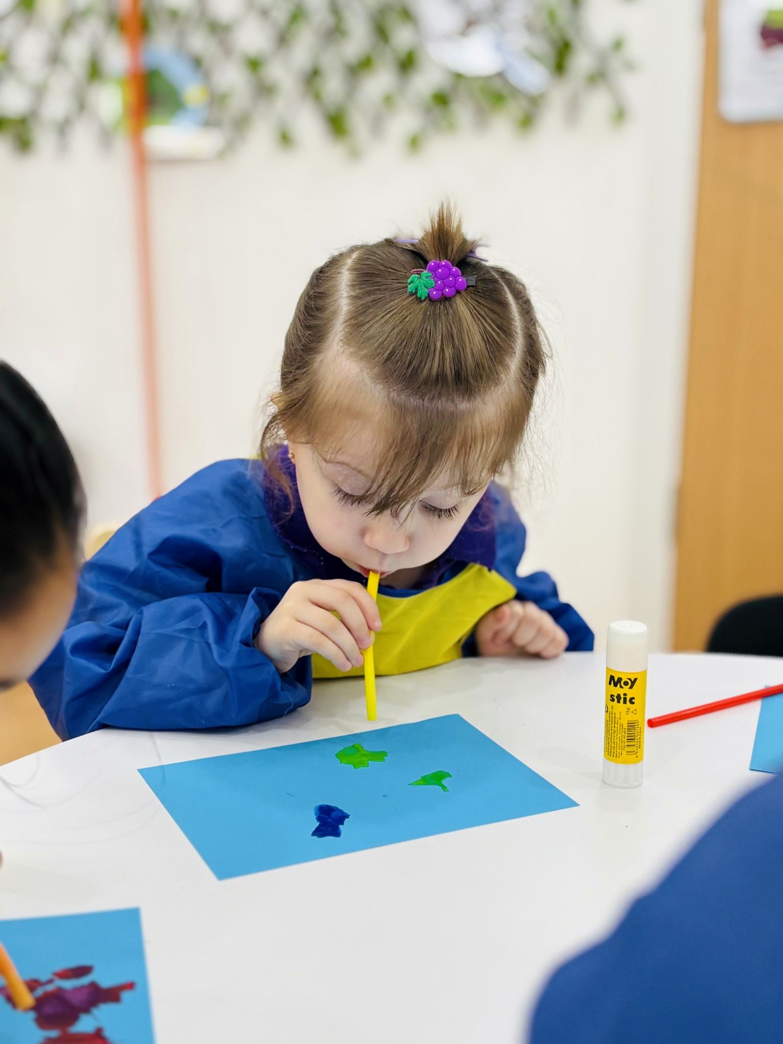Child creating colourful artwork by blowing paint through a straw