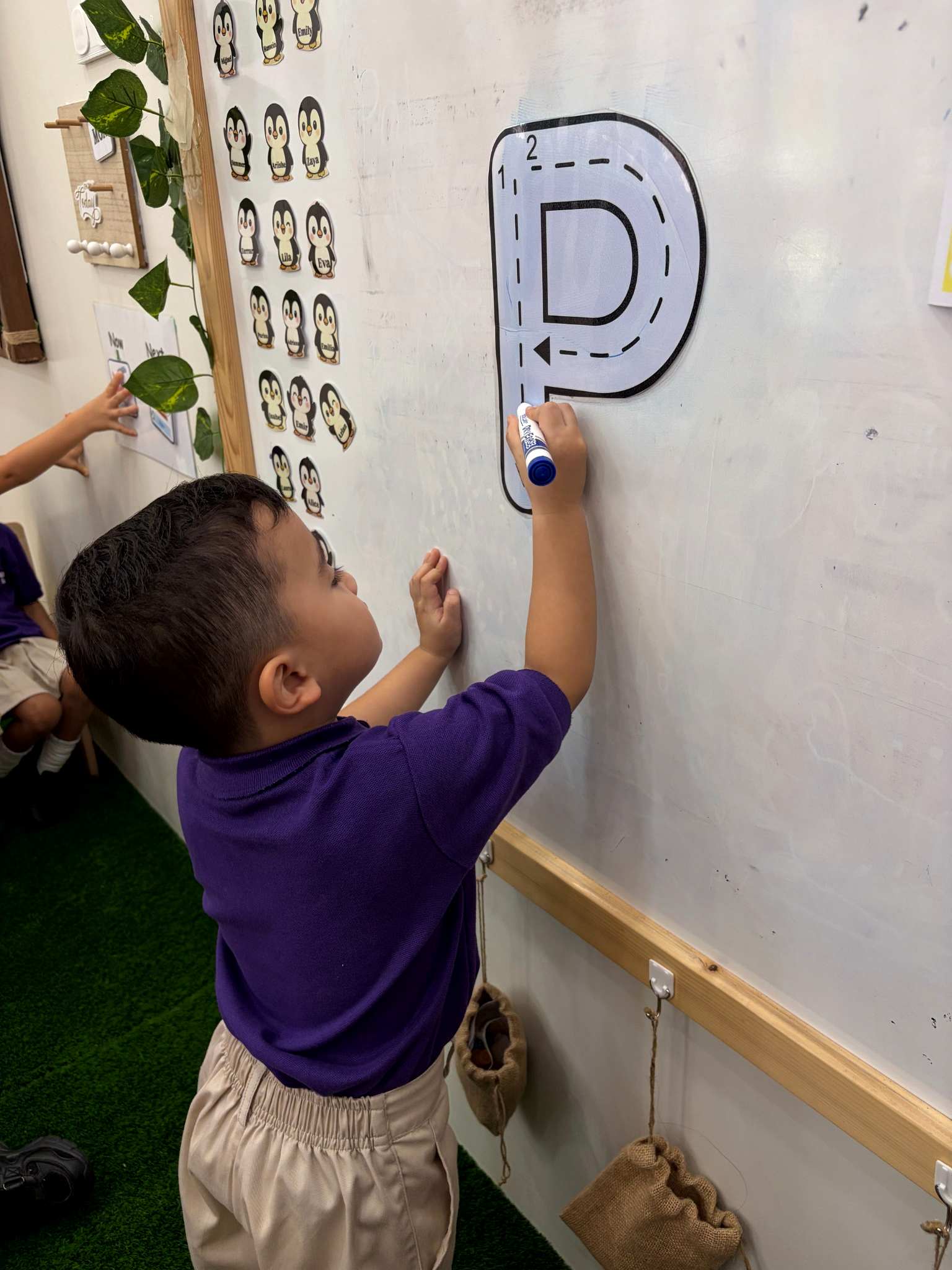 Child in nursery uniform tracing a large letter on a classroom board